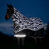 Horse wearing a black and white patterned rug with reflective strip at night.